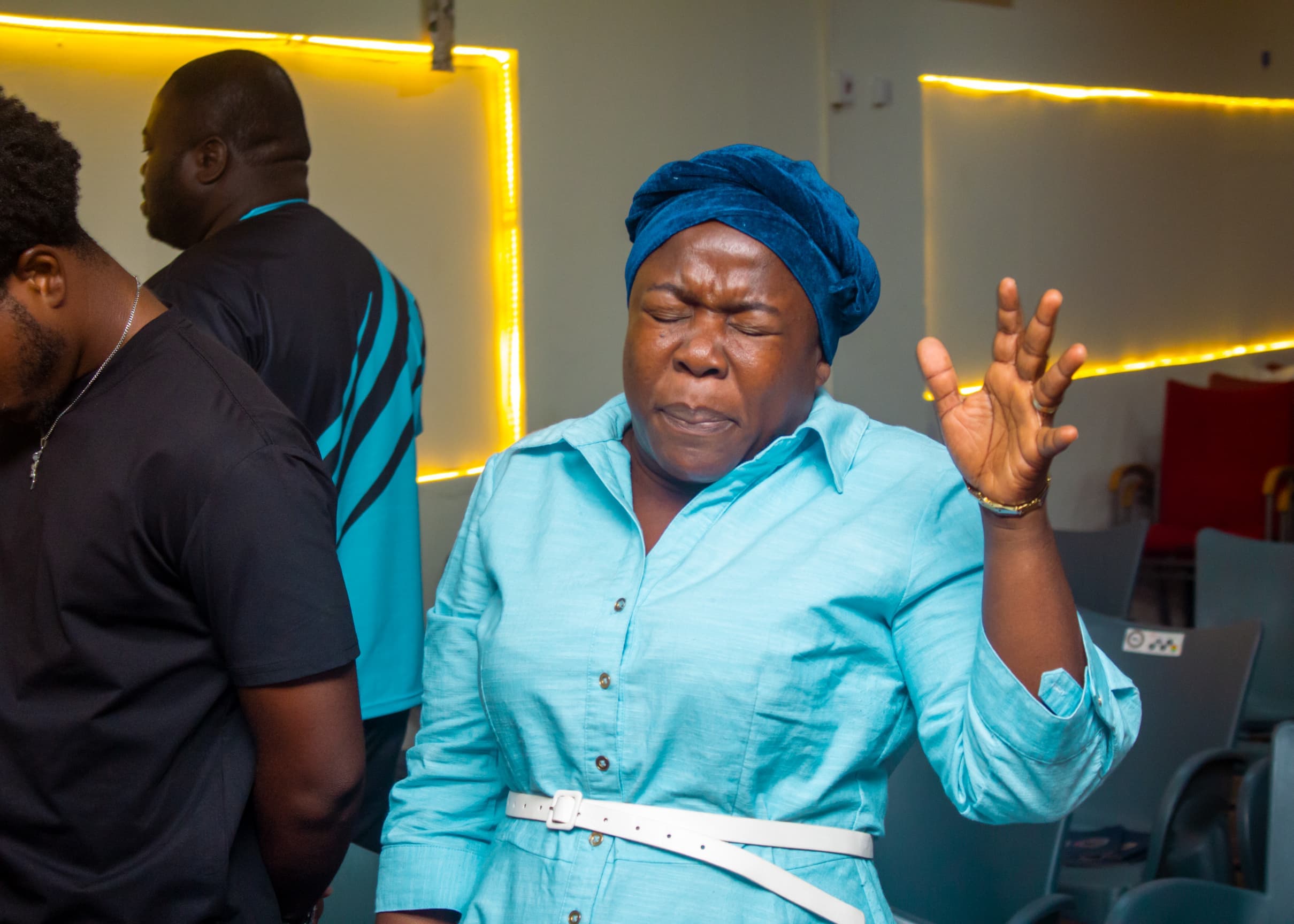 Woman in blue dress and headwrap worshipping during a service