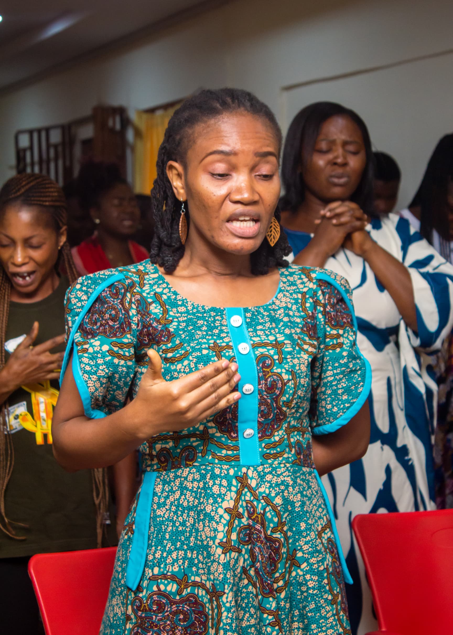 Woman in teal Ankara dress worshipping during a service