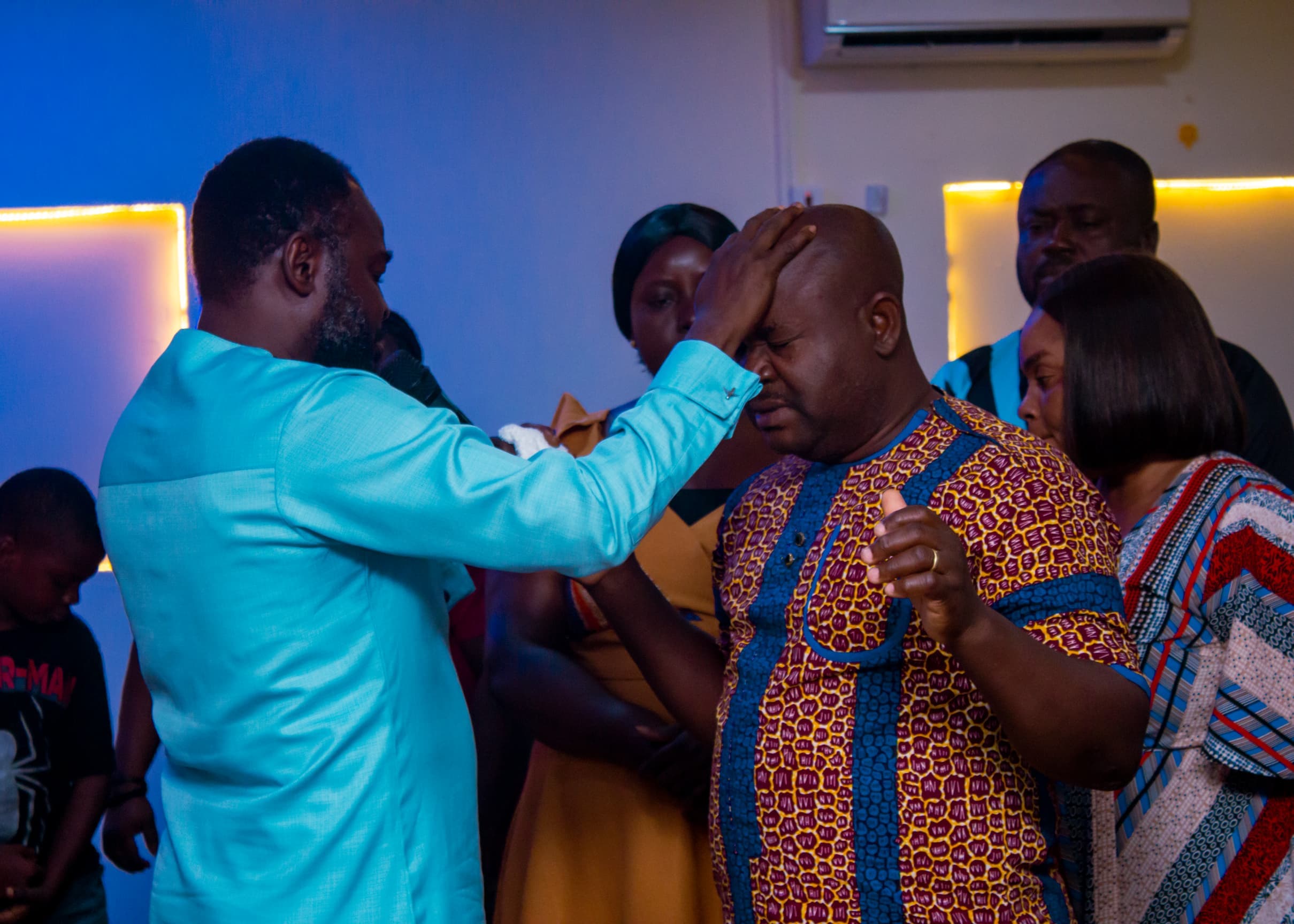 Apostle Benjamin Asamoah praying for a man in patterned attire