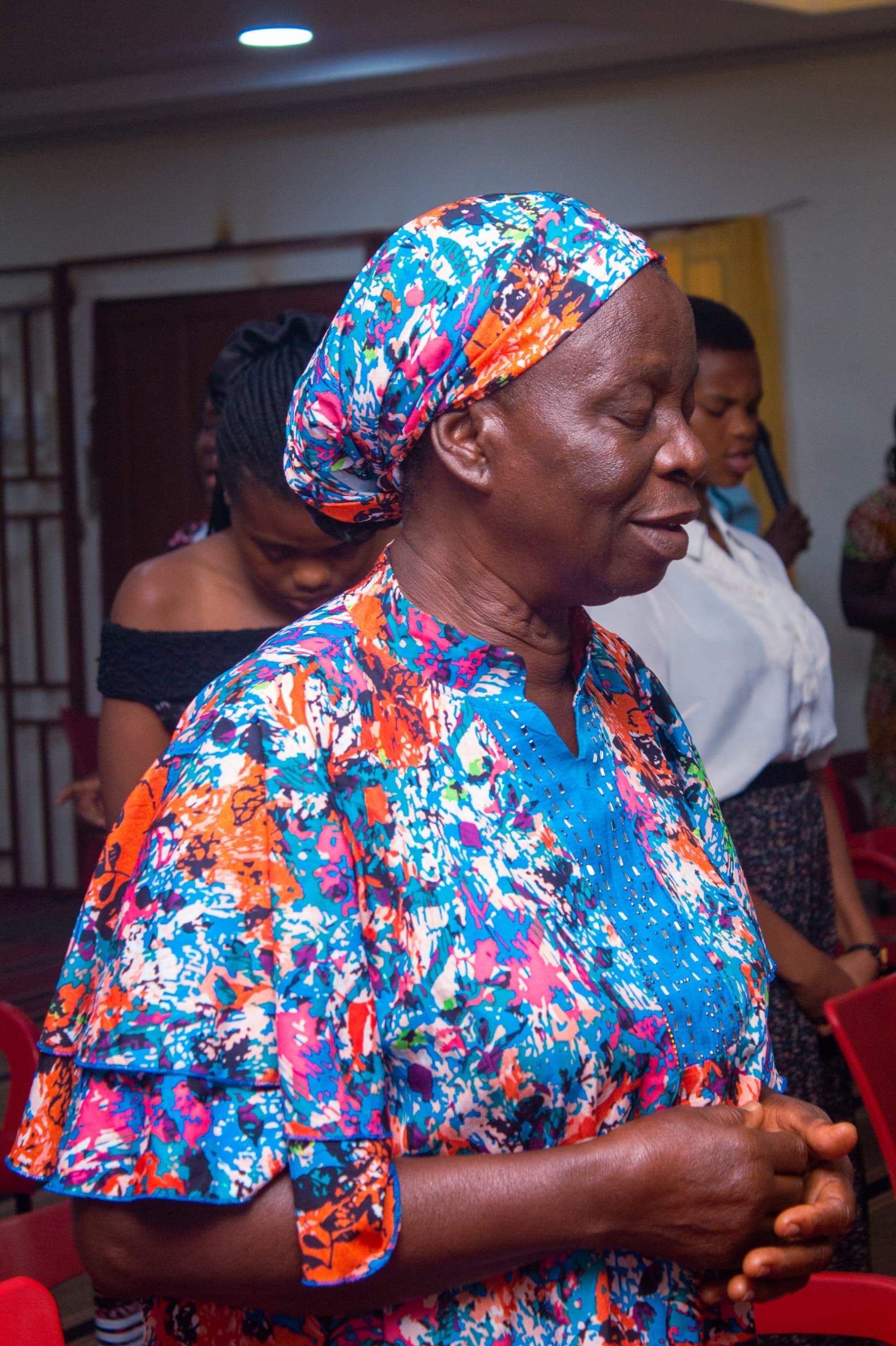 Elderly woman in colorful Ankara praying during worship